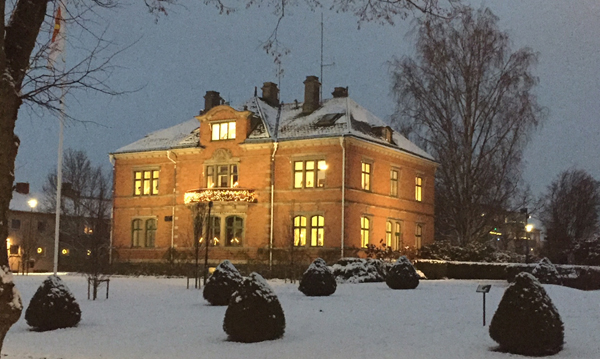 Ett tegelhus där det lyser ur alla fönster och det är snö runt. Huset är Katrineholms kommunhus, Gröna kulle.